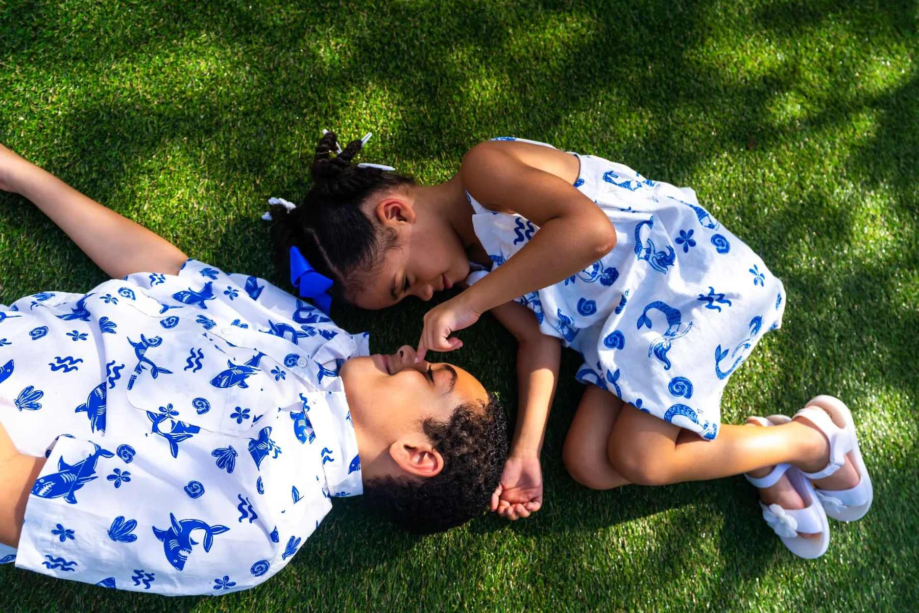 A young girl touching her brother’s nose as they lie together in the grass