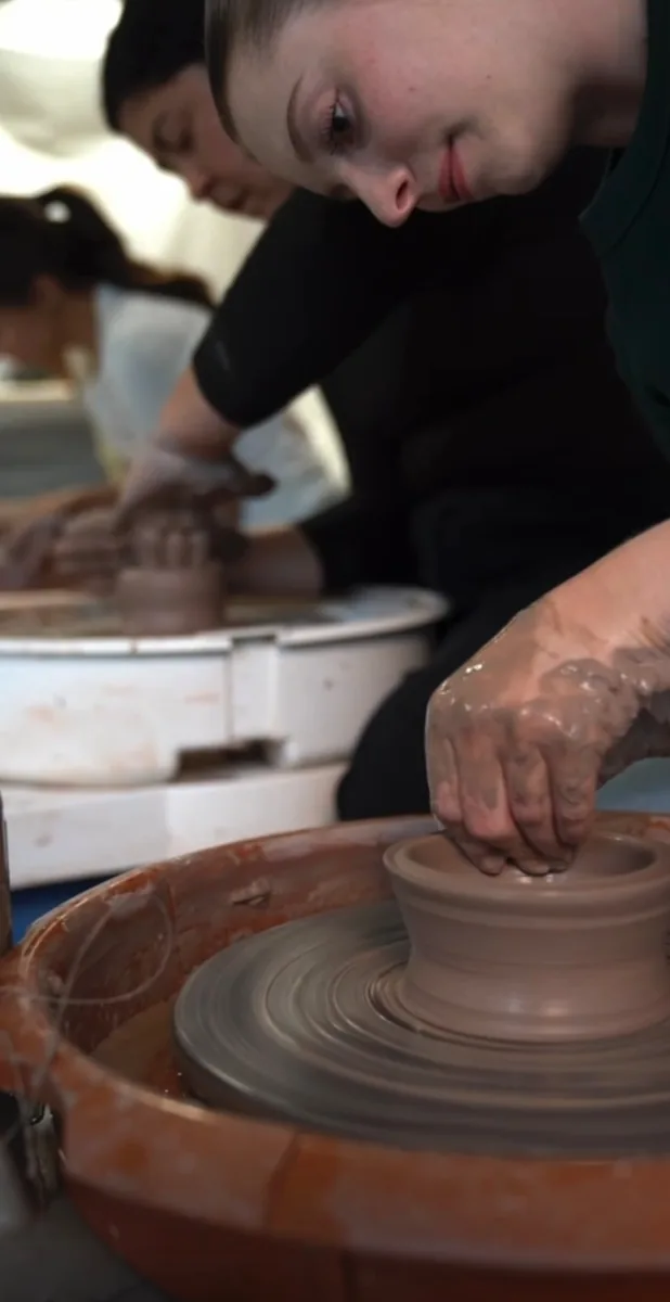 A potter working at a wheel with other people in the studio.