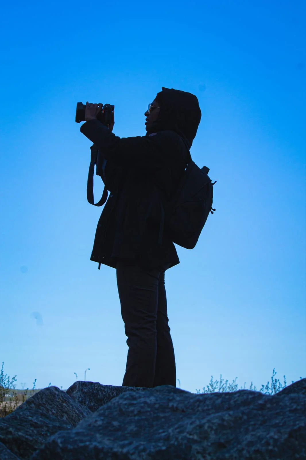 Silhouette of Zxamara Jester shooting with a camera against a blue sky