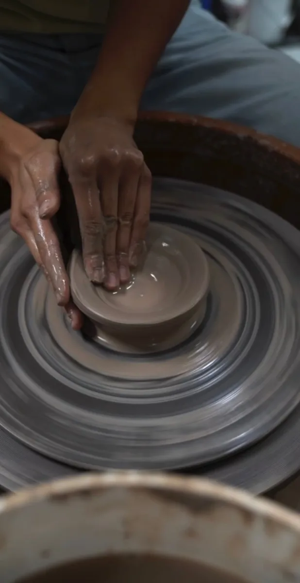 Overhead view of hands shaping clay on a spinning pottery wheel.