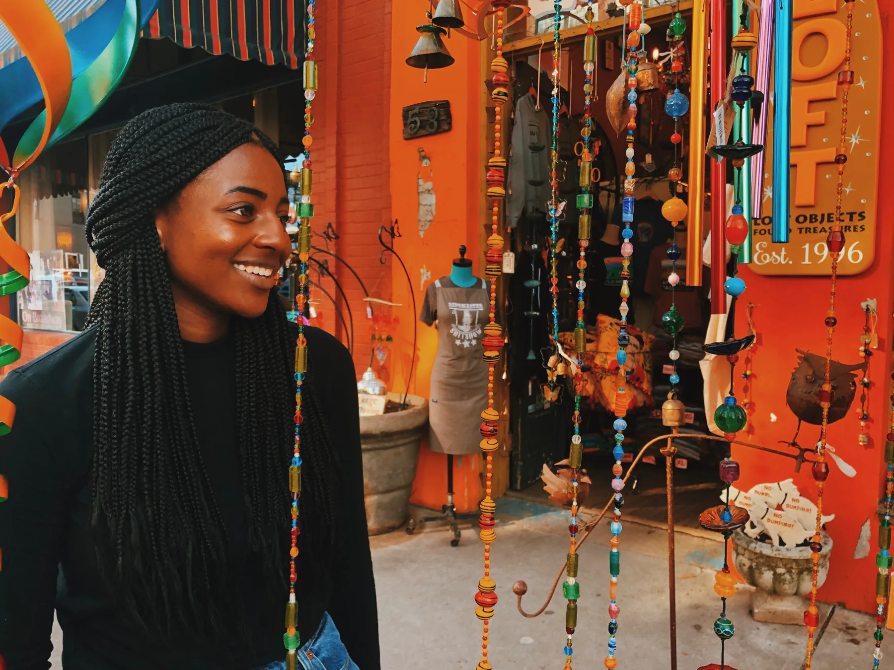 Zxamara Jester smiling beside colorful hanging beads outside a shop