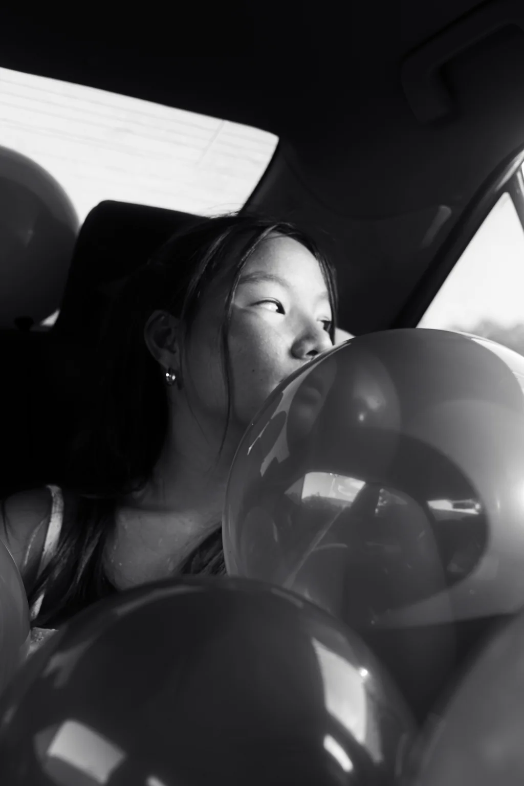 Black and white portrait of a young woman in a car surrounded by balloons