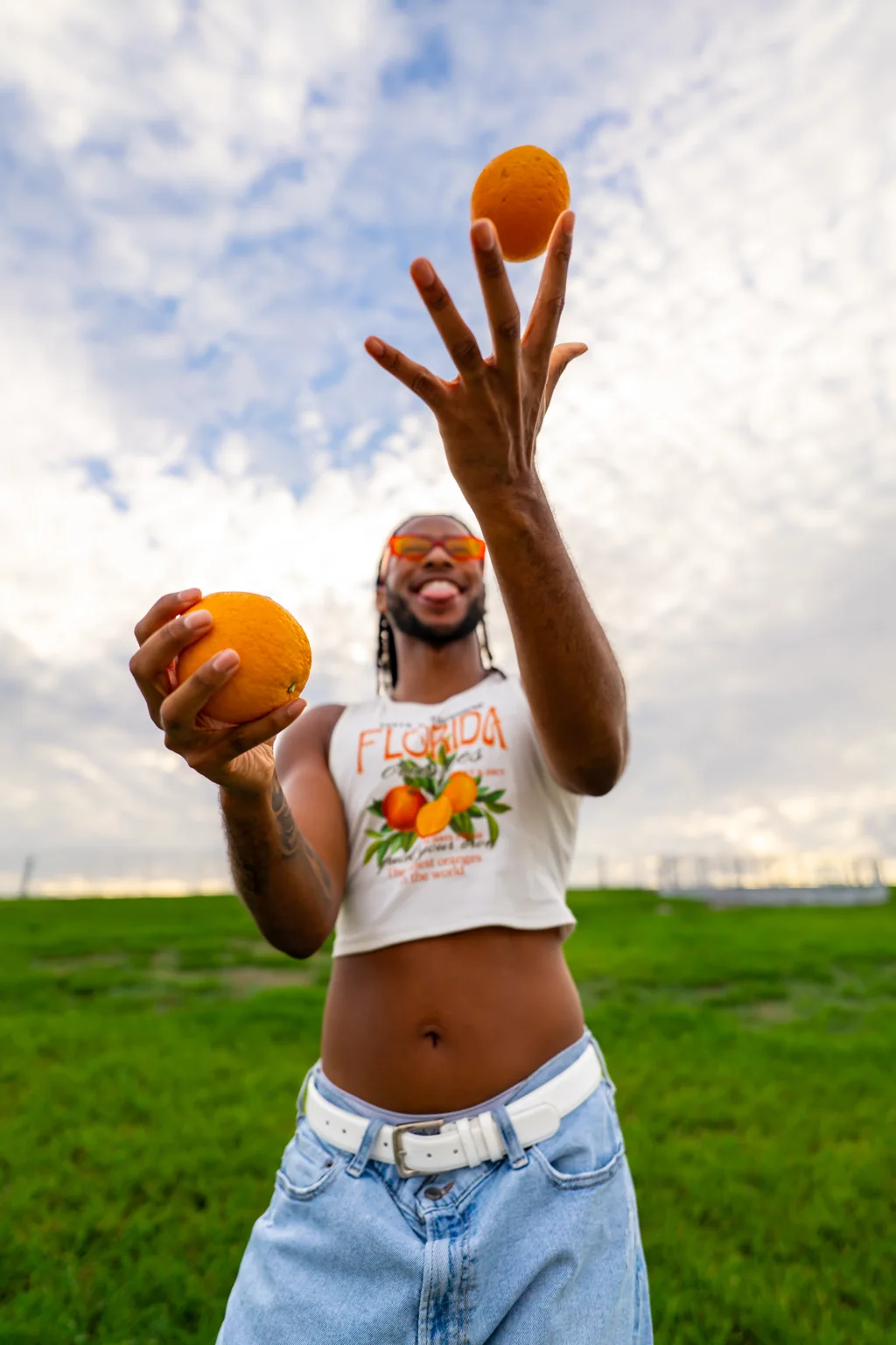 A man in orange sunglasses tossing oranges against a bright sky
